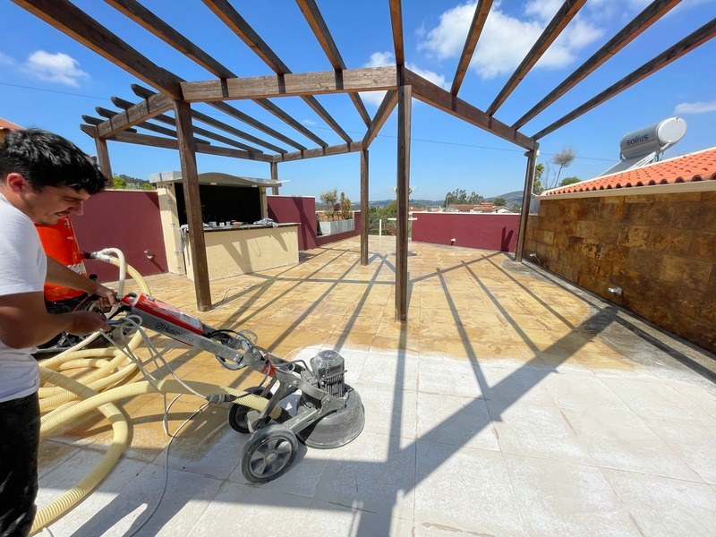 Trabalhador a lixar a tijoleira de um terraço com uma máquina de disco