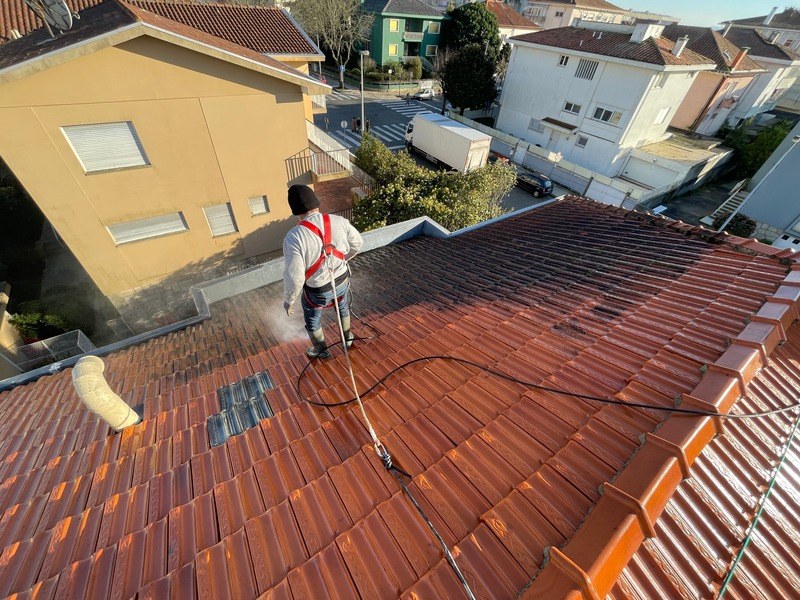 Trabalhador de arnês a lavar um telhado de telha